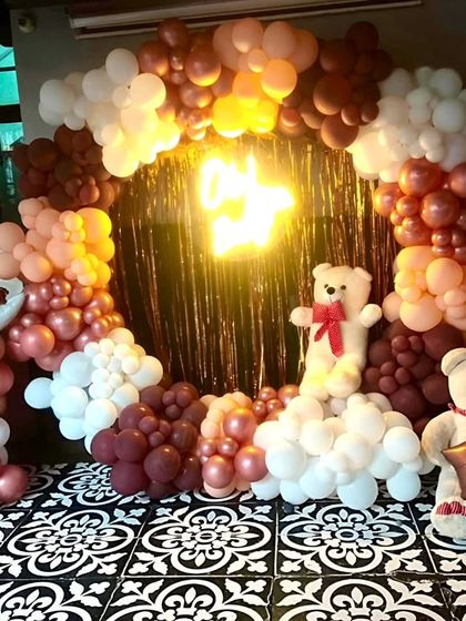 A beary special celebration! This cozy and cute teddy bear themed setup features a circular backdrop with a golden fringe, surrounded by a garland of white, brown, and rose gold balloons.