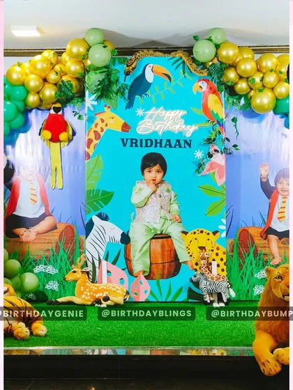 The centerpiece of this jungle party is the custom backdrop featuring the birthday boy's photo, surrounded by illustrated animals. Life-like animal props like a lion, leopard, and deer are placed in the foreground to create a layered, three-dimensional scene.