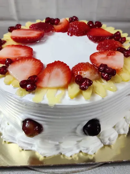 A fresh fruit cake decorated with sliced strawberries, pineapple, pomegranate, and cherries. A colorful and healthy choice.