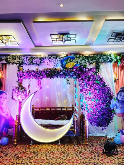 A beautiful baby shower stage with a peacock-themed floral decoration over a traditional swing and a lighted moon prop, creating a rich and elegant look.