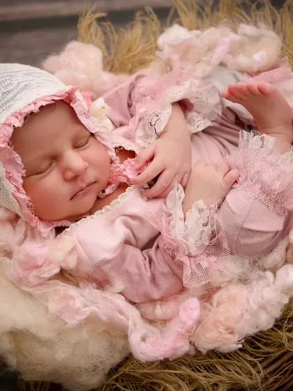 Dressed in an elaborate pink ruffled outfit and bonnet, this newborn sleeps in a rustic nest, looking like a character from a vintage storybook.