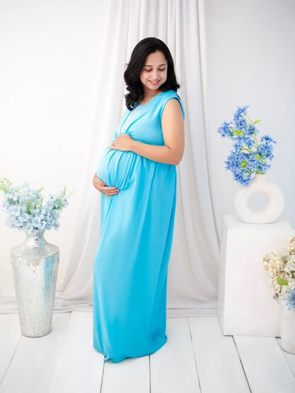 Simplicity and serenity. Dressed in a flowing sky-blue gown, the mother-to-be cradles her bump in our minimalist white studio setup. This clean, bright style creates a feeling of peace and pure anticipation.