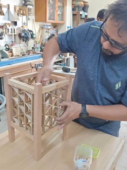 A student carefully fits the infill pieces into a triangle grid Kumiko lamp. This step requires precision and a gentle touch to ensure all parts interlock perfectly without glue or nails.