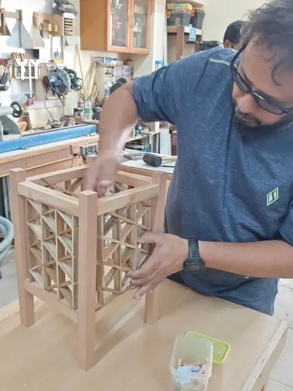 A student carefully fits the infill pieces into a triangle grid Kumiko lamp. This step requires precision and a gentle touch to ensure all parts interlock perfectly without glue or nails.