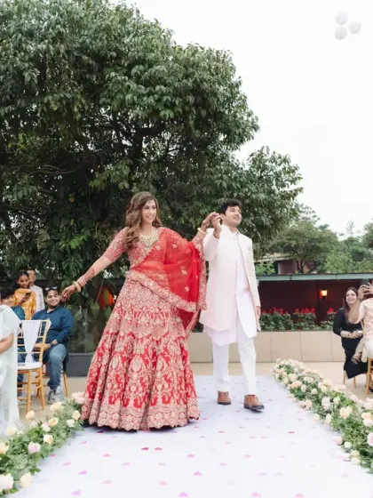 Hand in hand, the couple walks down the aisle as guests cheer and white balloons are released. The bride's red lehenga is a vibrant splash of colour in this joyous, celebratory moment.