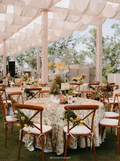 Dining tables at the Haldi, draped in lemon-print tablecloths and surrounded by wooden cross-back chairs adorned with small floral bouquets.