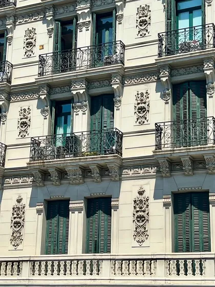 The beautiful facade of a building in Spain, with its rhythmic arrangement of balconies, shutters, and decorative carvings. The symmetry and attention to detail are a masterclass in classical architecture and timeless elegance.