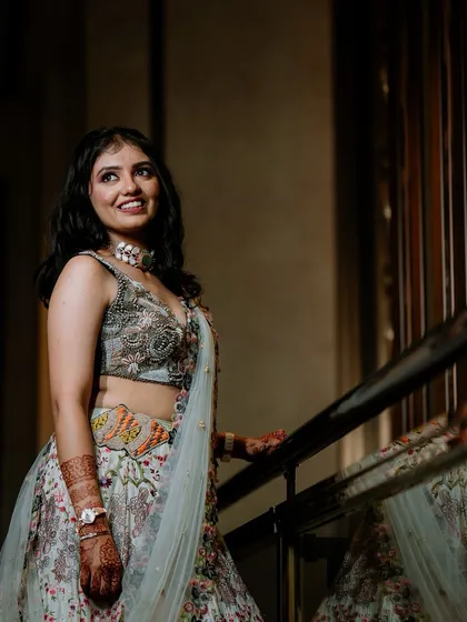 A full-length portrait of the bride in her floral lehenga, posing elegantly on a staircase.