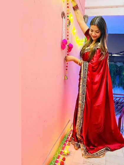 A glimpse from Diwali, decorating the house in my self-designed red satin saree. The custom "Sada Saubhagyavati Bhava" border adds a personal and traditional touch.