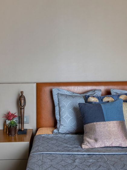 A wider shot of the bed in the Filigree House, showing the full effect of the layered blue pillows against the warm leather headboard. The design is simple, yet sophisticated.