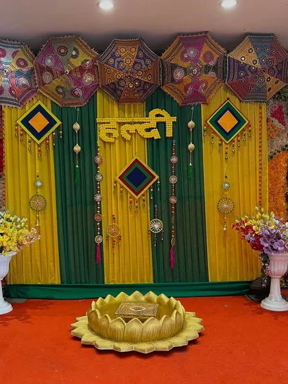 A vibrant Haldi stage with a mix of yellow and green drapes, Rajasthani umbrellas, and floral arrangements, creating a lively and traditional look.