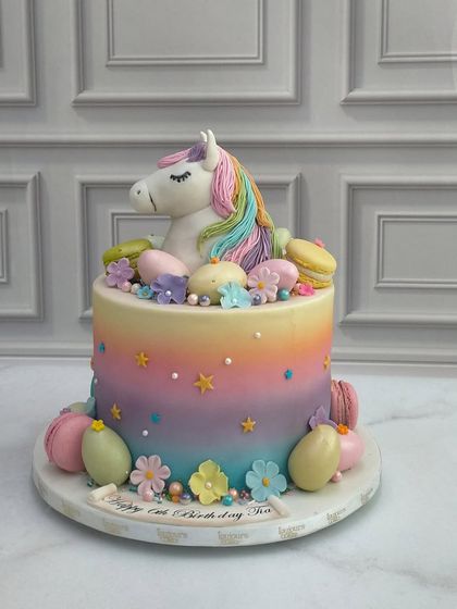 A magical unicorn cake with a rainbow pastel gradient. This design is adorned with a sculpted unicorn, colorful macarons, and whimsical stars, perfect for a fantasy-themed birthday celebration.