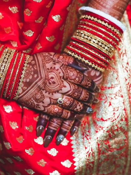 A close-up of a bride's hands against her red saree, highlighting the beautiful heart-shaped design on the back of her hand.