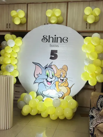 A classic Tom & Jerry theme for a 5th birthday. The simple setup uses a large circular backdrop with the iconic duo, framed by yellow and white balloons for a clean, fun look.