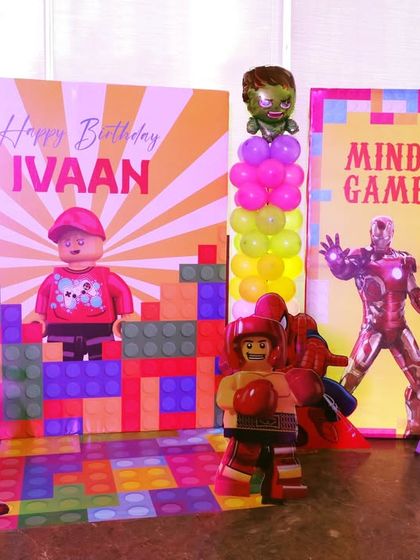 A LEGO and Superheroes themed party with a brick-patterned backdrop and cutouts of Iron Man and a LEGO character.