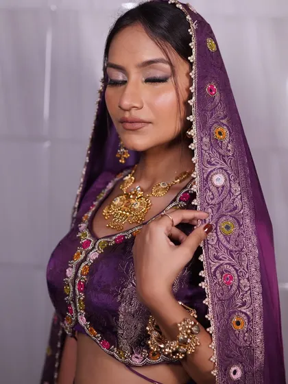 A serene and elegant portrait of a bride in a rich purple outfit. The makeup focuses on sculpted eyes and a radiant base, creating a look of effortless grace.