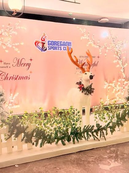 A festive 'Merry Christmas' photo backdrop for Goregaon Sports Club. The winter wonderland scene includes flocked trees, a decorative reindeer, and a white picket fence, creating a perfect holiday photo opportunity.