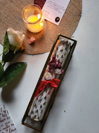 The final presentation of a scroll letter in its glass and brass box, tied with a red ribbon and adorned with dried flowers.