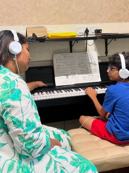 A mother and son learn piano together with headphones. We love seeing families bond over music and support each other's learning journey.