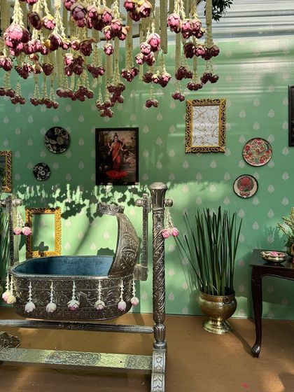 The ornate silver cradle, decorated with delicate pink floral tassels, awaits the baby. The backdrop features a custom-printed wall and hanging lotus buds.