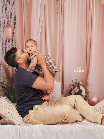 A heartwarming moment between a father and his baby during a sitter session. The gentle kiss and the baby's happy smile are perfectly captured in our cozy, boho-themed studio setup.
