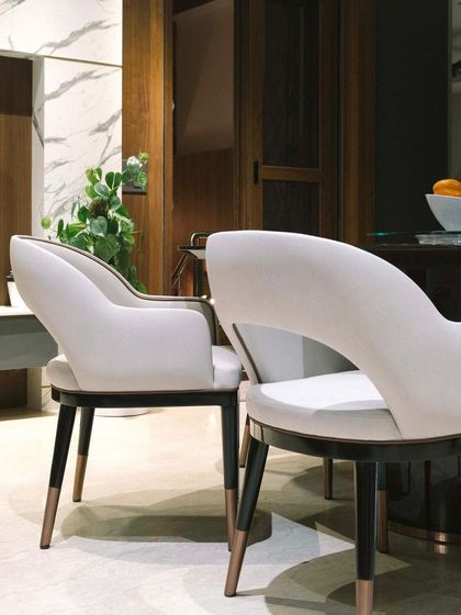 The elegant, curved back of these dining chairs, upholstered in a soft, neutral fabric, exemplifies our selection of furniture that combines comfort with sculptural beauty.