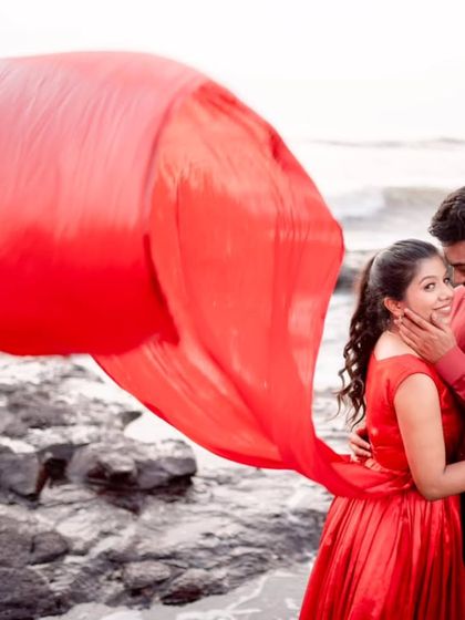 A happy, intimate moment captured beautifully. The red gown's trail swirls around the couple, adding a dynamic element to this romantic beachside portrait.