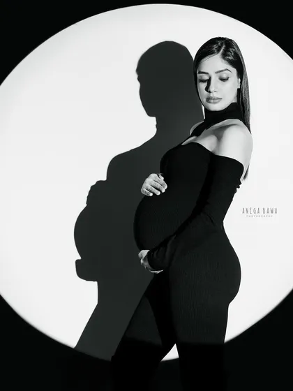 A modern and graphic black and white portrait. Using a single spotlight, we create a strong silhouette and shadow play for a bold, high-fashion maternity look.