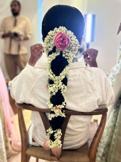 A behind the scenes shot of a bride in the chair, her hair styled in a beautiful jasmine and rose braid, ready for her big moment.