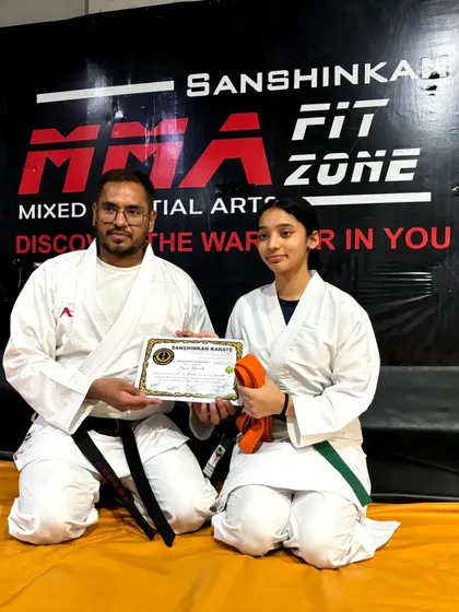 A young girl receives her green and orange belts, showing her dedication and progress in our karate program.