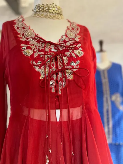A closer look at the craftsmanship. This red peplum top features intricate floral embroidery with a delicate tie-up detail at the neckline, adding a touch of romance.
