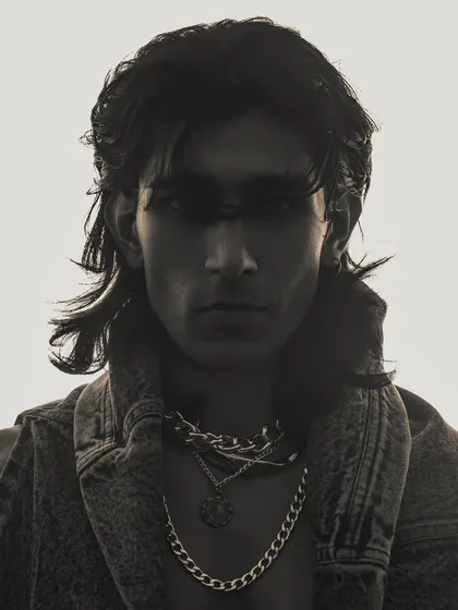 A high-contrast, silhouette-style portrait of a male model. The backlighting obscures his features, creating a mysterious and moody image that focuses on his striking hair and profile.