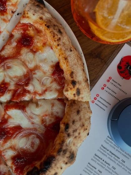 The perfect setup: our Goan Sausage pizza, the menu, a cool drink, and some tunes.