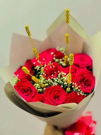 A simple and beautiful bouquet of red roses, accented with golden decorative sticks for a unique touch. The kraft paper wrapping gives it a natural and rustic charm.