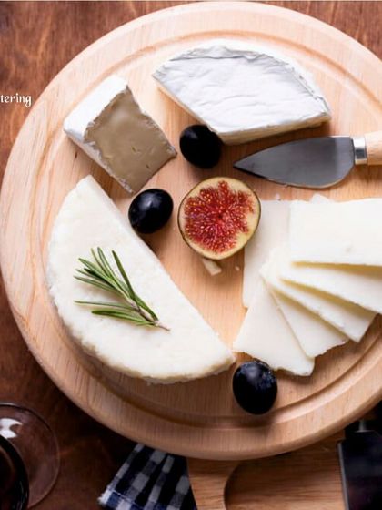 An overhead shot of a simple yet elegant cheese board with various cheeses, fresh figs, and grapes. The arrangement on the round wooden board is clean and visually appealing.