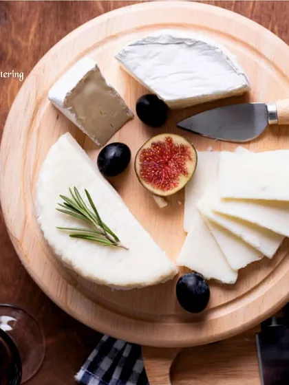 An overhead shot of a simple yet elegant cheese board with various cheeses, fresh figs, and grapes. The arrangement on the round wooden board is clean and visually appealing.