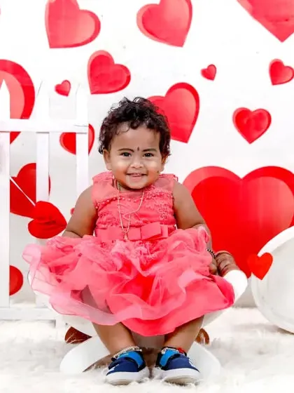 Celebrating love with a Valentine's Day themed photoshoot. This sweet little girl is all smiles in a pink dress, surrounded by a backdrop of red and white hearts.