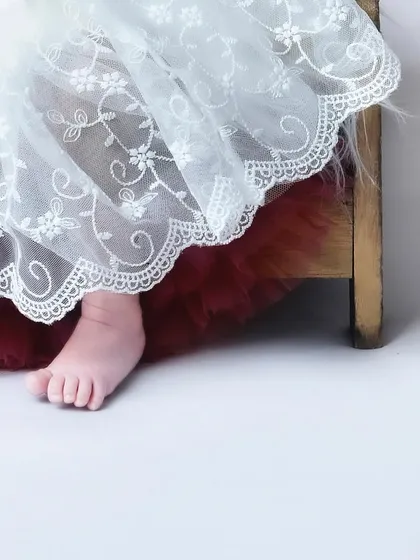A sweet detail shot of a newborn's foot peeking out from under a delicate white lace dress. It’s a subtle and beautiful way to capture their tininess.