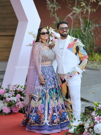 A stylish couple poses on the red carpet at their wedding event. Their modern, colorful outfits and cool sunglasses make for a unique wedding portrait.