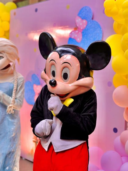 A close-up of the Mickey Mouse mascot at a party, with Queen Elsa in the background. Having multiple characters adds to the excitement and provides more interactive fun for the children.