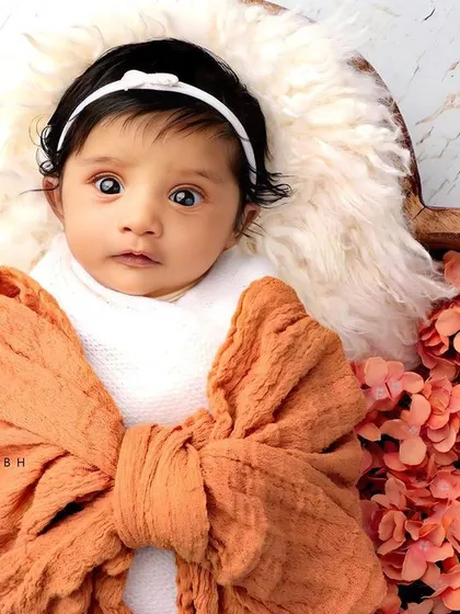 An alert and curious baby looking up from a heart-shaped wooden bowl, wrapped like a little gift.