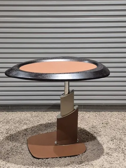 This modern side table has a unique, sculptural base and a mixed-material top, combining metal and leatherette.