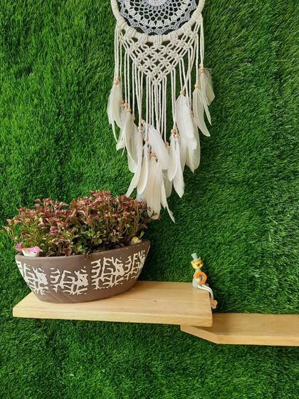 Detail shot of the floating shelf on the green wall, featuring a patterned ceramic planter, a whimsical frog figurine, and a beautiful macrame dreamcatcher. It's these small touches that bring a space to life.