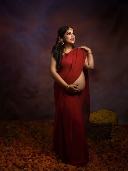 A portrait of grace. This standing pose in a red saree, surrounded by marigolds, is a timeless tribute to Indian traditions and the strength of motherhood.