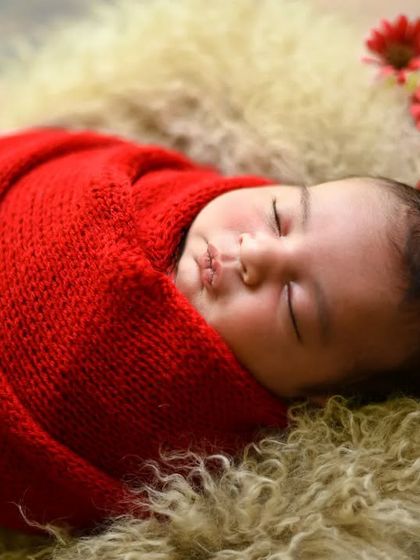 A close-up portrait focusing on the baby's peaceful face while swaddled in a vibrant red wrap.
