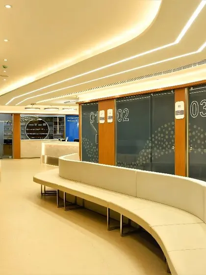 The waiting corridor in the eye hospital features a long, curved bench and clearly numbered consultation rooms. This spatial design facilitates easy patient flow and enhances comfort during their visit.