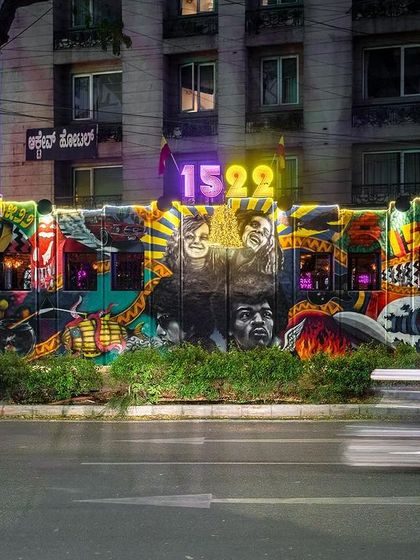 A motion-blurred shot of the 1522 The Pub facade at night. The colorful mural and bright neon sign make it a dynamic part of the urban landscape.