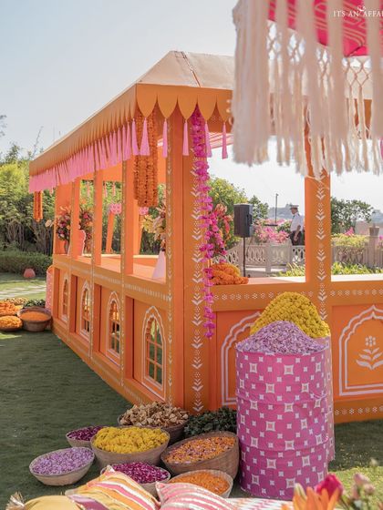 A food or activity stall designed with Rajasthani architectural details, complete with hanging floral garlands and baskets of fresh flower petals.