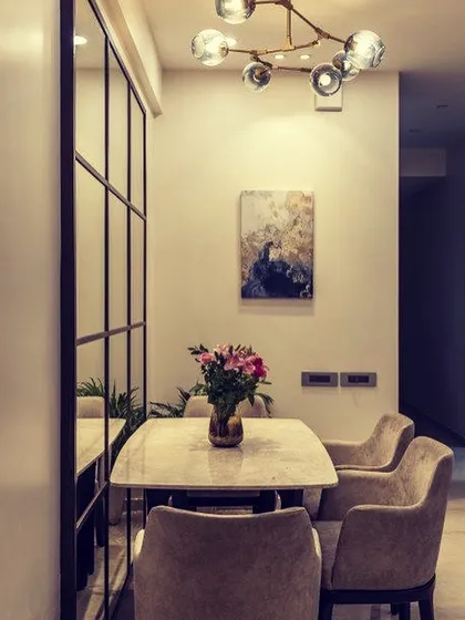 A cozy dining nook with a marble table, comfortable upholstered chairs, and a modern bubble chandelier. The large grid mirror on the wall adds an industrial-chic element to the design.