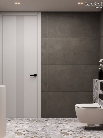 This angle shows how the different elements of the bathroom come together. The terrazzo-style tile on the floor and half-wall provides continuity, while the large grey tiles create a calm backdrop. The clean lines of the pedestal sink and the simple white door maintain the room's modern, uncluttered feel.